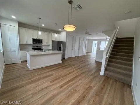 Kitchen with appliances with stainless steel finishes, a center island with sink, white cabinetry, and hardwood / wood-style flooring