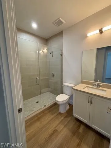 Bathroom with an enclosed shower, toilet, vanity, and wood-type flooring