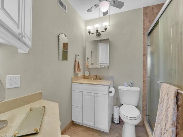 Full bathroom featuring vanity, toilet, a ceiling fan, a shower stall, and baseboards