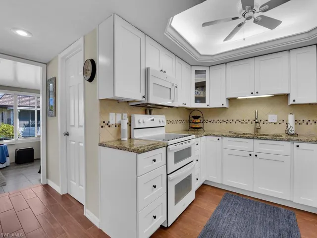Kitchen with white appliances, a sink, stone counters, a ceiling fan, and glass insert cabinets