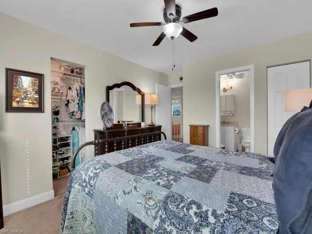 Carpeted bedroom with a walk in closet, baseboards, a closet, connected bathroom, and ceiling fan