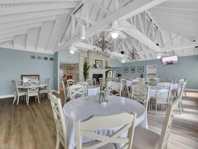 Dining room with a ceiling fan, high vaulted ceiling, a stone fireplace, baseboards, and wood finished floors