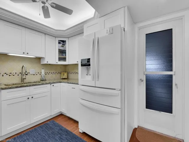 Kitchen featuring white refrigerator with ice dispenser, a sink, dark wood-type flooring, ceiling fan, and light stone countertops