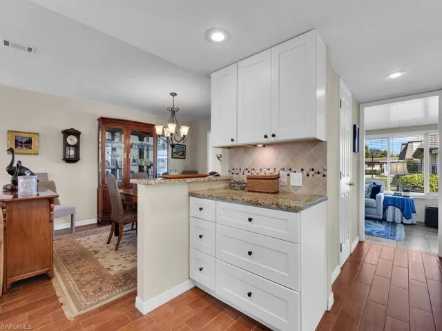 Kitchen featuring wood finish floors, a chandelier, baseboards, light stone counters, and white cabinetry