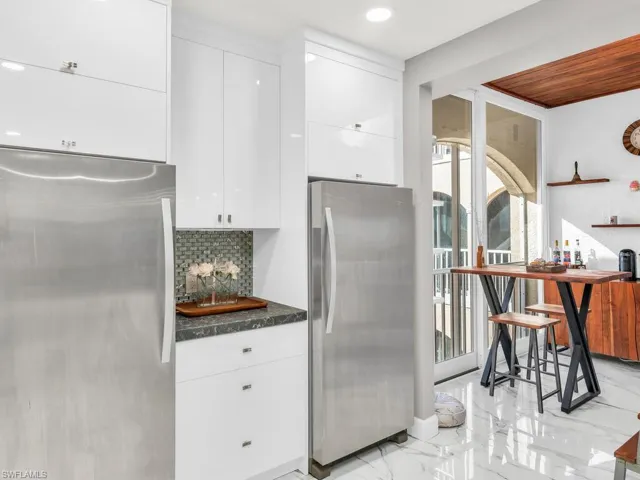 Kitchen featuring dark stone counters, stainless steel fridge, white cabinetry, and backsplash