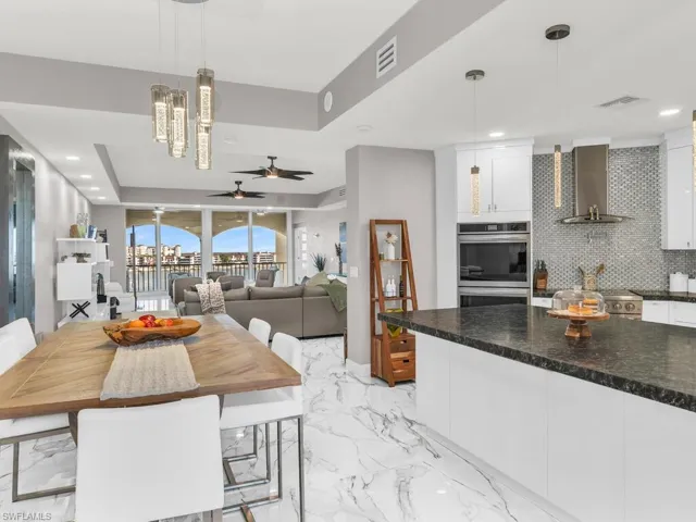 Kitchen with white cabinetry, hanging light fixtures, double oven, wall chimney range hood, and decorative backsplash