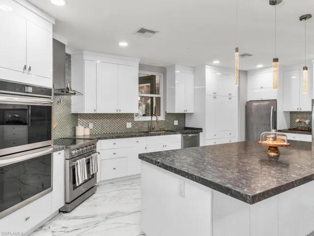 Kitchen featuring stainless steel appliances, a center island, white cabinets, decorative backsplash, and wall chimney range hood