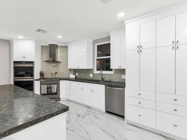 Kitchen featuring white cabinets, decorative backsplash, appliances with stainless steel finishes, and wall chimney exhaust hood