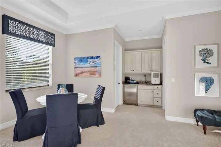 Dining room featuring light colored carpet, wet bar, and ornamental molding