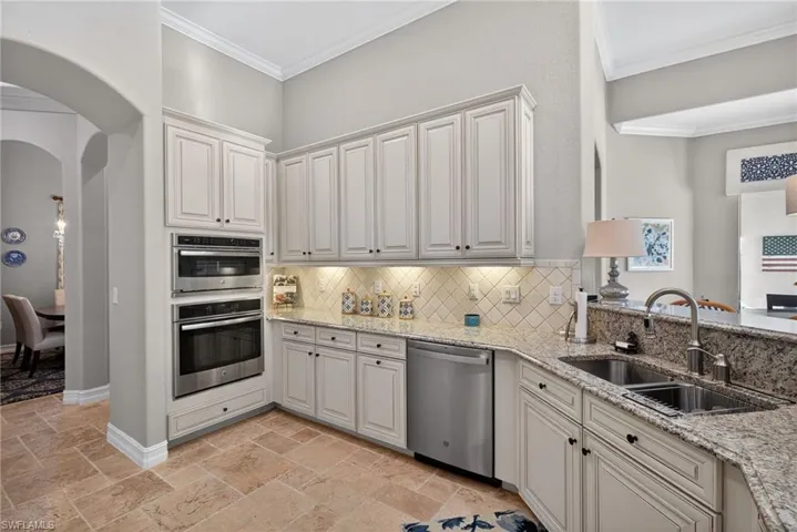 Kitchen with arched walkways, appliances with stainless steel finishes, crown molding, light stone counters, and stone tile floors