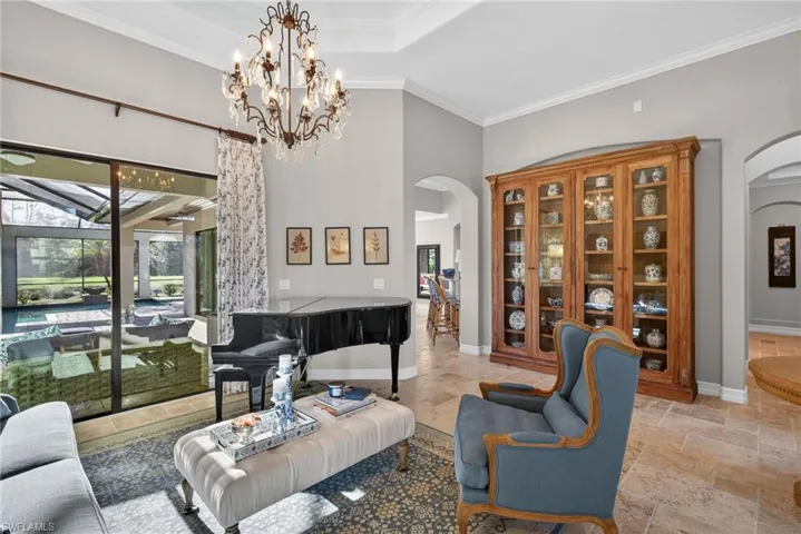 Living area featuring stone tile floors, ornamental molding, a towering ceiling, a chandelier, and arched walkways