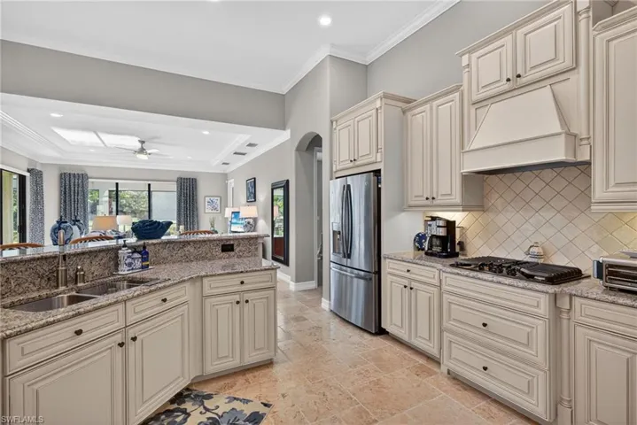 Kitchen with cream cabinets, light stone counters, ornamental molding, stainless steel refrigerator with ice dispenser, and stone tile floors