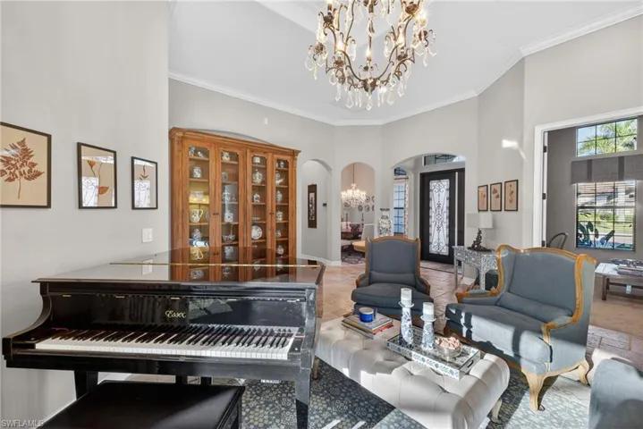 Living area with a chandelier, arched walkways, a towering ceiling, ornamental molding, and plenty of natural light