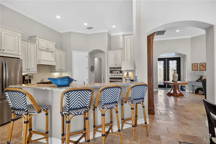 Kitchen with arched walkways, light stone counters, ornamental molding, decorative backsplash, and appliances with stainless steel finishes