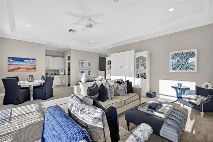 Living area with ceiling fan, a tray ceiling, carpet flooring, recessed lighting, and ornamental molding