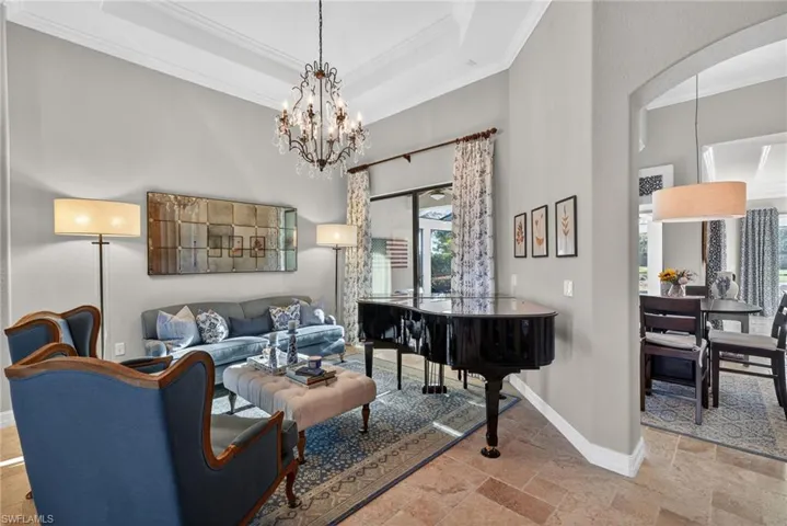 Living area with ornamental molding, a high ceiling, stone tile flooring, a tray ceiling, and a chandelier