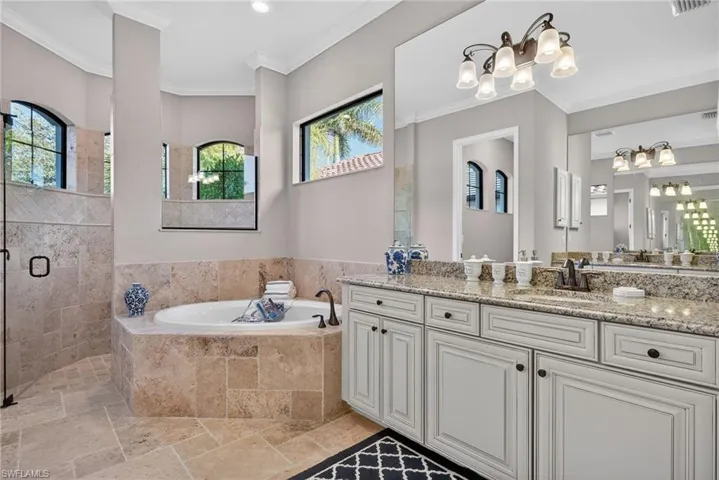 Bathroom with stone tile floors, crown molding, a garden tub, vanity, and a shower stall
