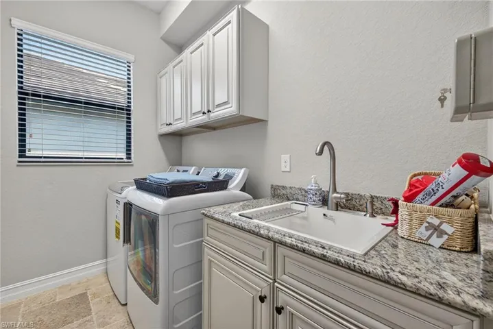 Washroom with a textured wall, washing machine and dryer, stone tile flooring, and cabinet space