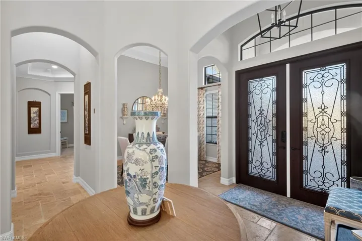 Entrance foyer featuring a chandelier, stone tile floors, ornamental molding, a high ceiling, and arched walkways