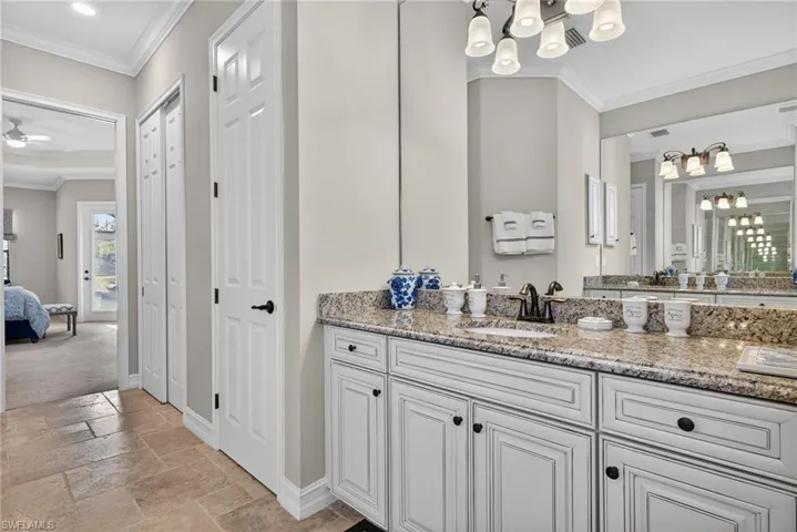 Ensuite bathroom featuring ornamental molding, vanity, stone tile flooring, a chandelier, and a closet