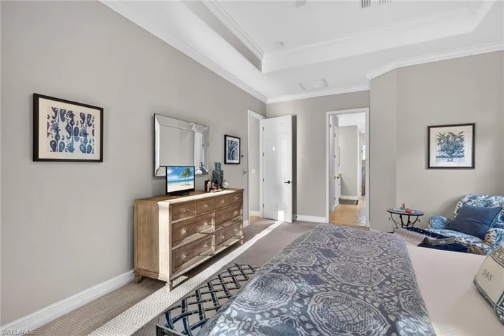 Bedroom featuring carpet flooring, ensuite bathroom, a raised ceiling, crown molding, and attic access