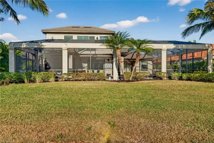 Rear view of house featuring a lawn, glass enclosure, and a sunroom