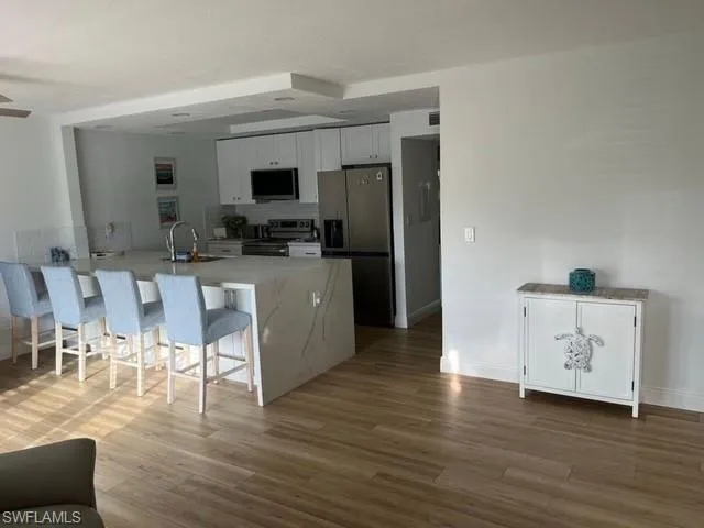 Kitchen featuring a kitchen bar, stainless steel appliances, wood finished floors, white cabinetry, and a sink