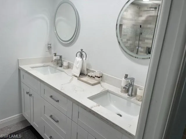 Full bathroom featuring double vanity, a shower stall, baseboards, and a sink