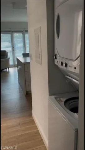 Laundry room with baseboards, laundry area, electric panel, stacked washer and dryer, and light wood-style floors