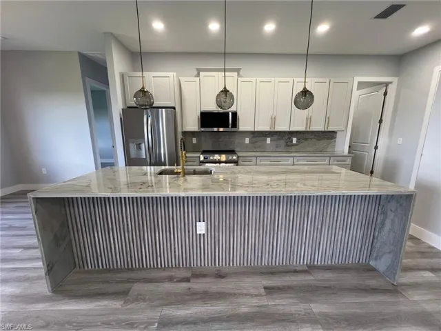 Kitchen featuring tasteful backsplash, stainless steel appliances, light stone counters, a large island, and hardwood / wood-style flooring