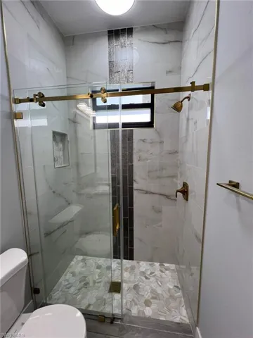 Bathroom featuring a shower with shower door and toilet