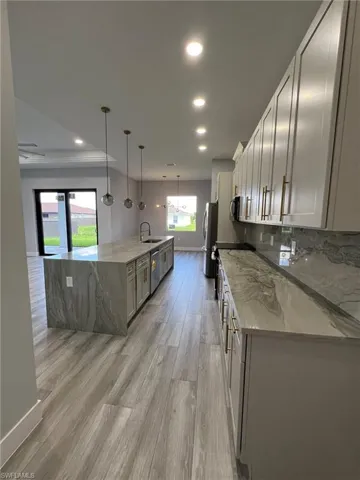 Kitchen with hanging light fixtures, light stone counters, a large island, and light hardwood / wood-style floors