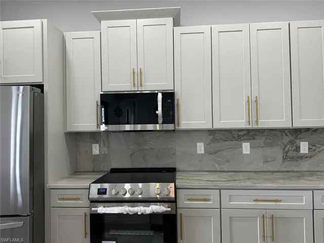 Kitchen with light stone countertops, white cabinets, backsplash, and stainless steel appliances