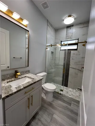 Bathroom featuring hardwood / wood-style floors, walk in shower, toilet, and large vanity