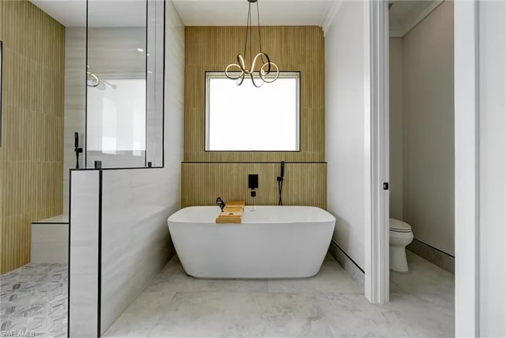 Full bath with walk in shower, a freestanding tub, tile walls, tile patterned flooring, and a chandelier