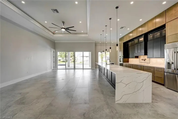 Kitchen with hanging light fixtures, a spacious island, ornamental molding, a tray ceiling, and light stone counters