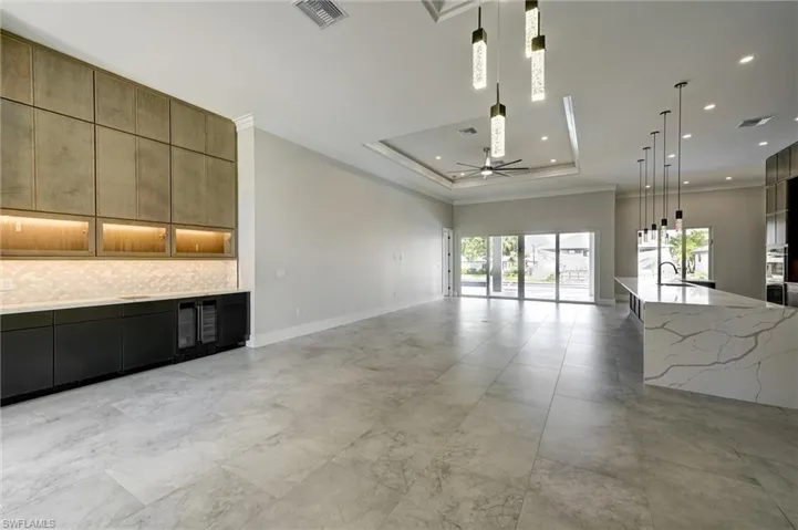 Kitchen with hanging light fixtures, modern cabinets, ornamental molding, a raised ceiling, and light stone countertops
