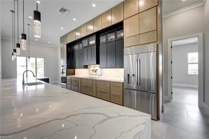 Kitchen with hanging light fixtures, light stone counters, appliances with stainless steel finishes, ornamental molding, and glass insert cabinets