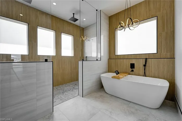 Bathroom with a freestanding tub, a walk in shower, tile walls, light tile patterned floors, and recessed lighting