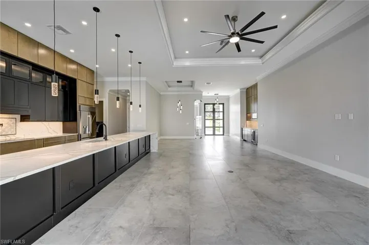 Kitchen featuring dark cabinets, decorative light fixtures, open floor plan, a raised ceiling, and light stone counters