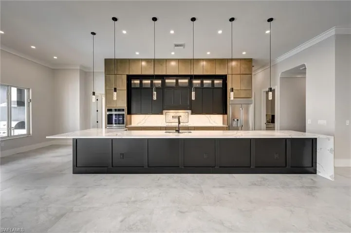 Kitchen with ornamental molding, light stone countertops, glass insert cabinets, a breakfast bar, and pendant lighting