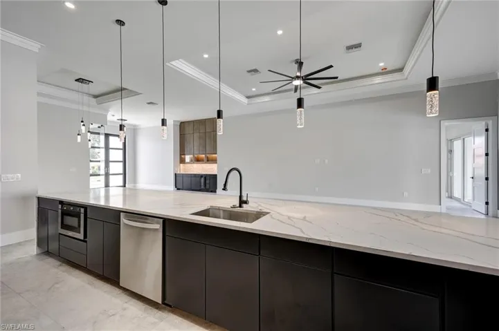 Kitchen featuring a tray ceiling, pendant lighting, modern cabinets, ornamental molding, and light stone counters