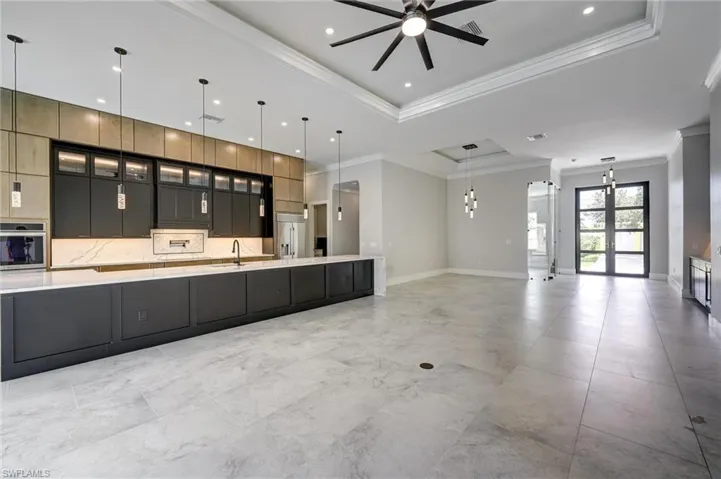 Kitchen featuring glass insert cabinets, a tray ceiling, hanging light fixtures, open floor plan, and dark cabinetry