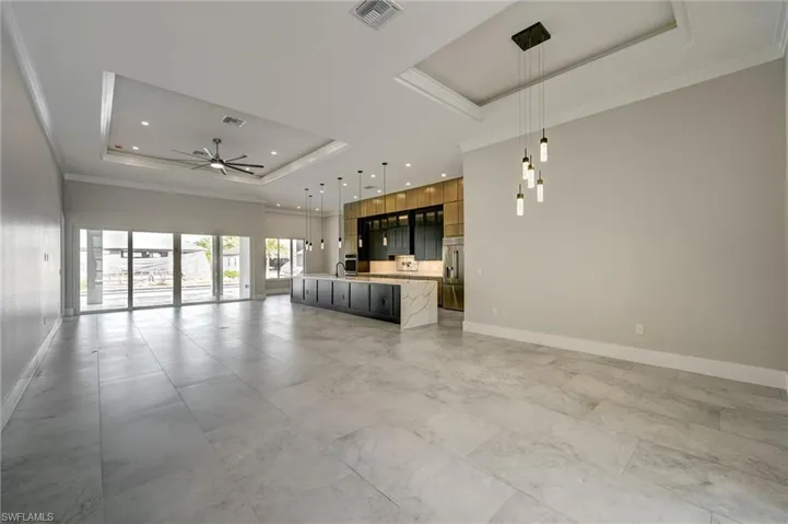 Unfurnished living room featuring a raised ceiling, ornamental molding, and ceiling fan
