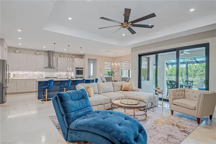 Living room featuring a ceiling fan, a raised ceiling, a chandelier, and concrete flooring
