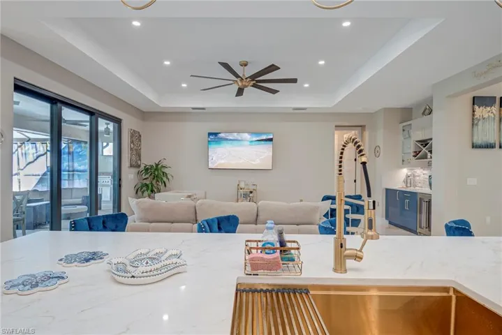Kitchen with open floor plan, a ceiling fan, light stone countertops, glass insert cabinets, and recessed lighting