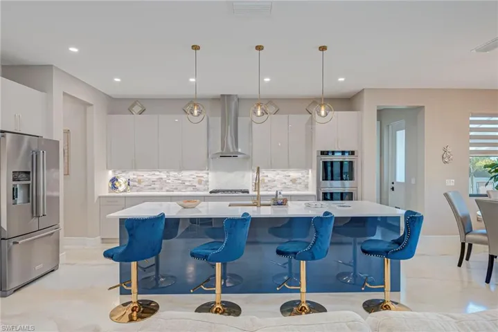 Kitchen with stainless steel appliances, white cabinetry, a breakfast bar area, light stone counters, and decorative light fixtures