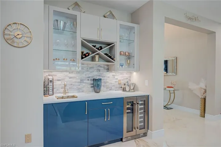 Indoor wet bar with beverage cooler, modern cabinets, dual tone cabinets, light stone counters, and decorative backsplash