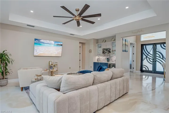 Living area featuring a bar, a tray ceiling, a ceiling fan, wine cooler, and concrete flooring
