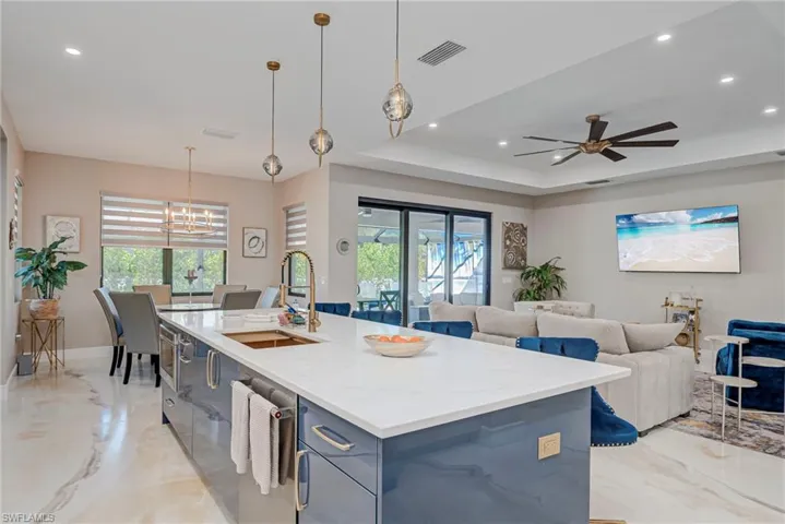 Kitchen featuring light stone countertops, an island with sink, open floor plan, ceiling fan, and blue cabinets